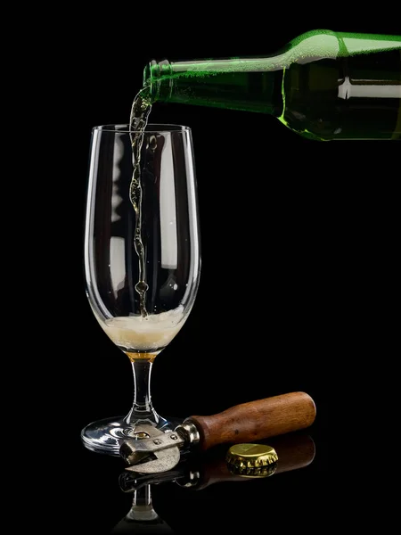 Filling of glass by beer from bottle is isolated on black