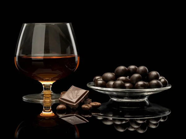 Cognac in glass and chocolate covered coffee beans — Stock Photo, Image