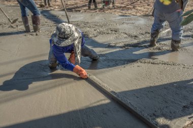 Adam oturmuş ve tahta bir spatula çimento için boşalırcasına hazır beton çelik takviye üzerinde sonra yolun karıştırılarak Mobil Beton Mikser yapmak kullanarak.