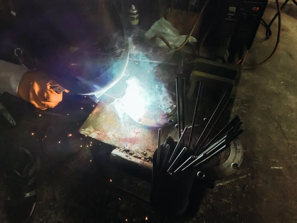 Close up worker welding steel with smoke and colourful of lights in industrial work shop.