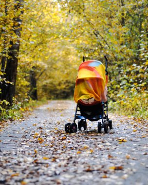 Bebek arabası küçük bir çocukla sokakta sonbahar ağaçlarıyla çevrili bir battaniye ile örtülü. Uyku ve temiz hava, açık havada yürümek.