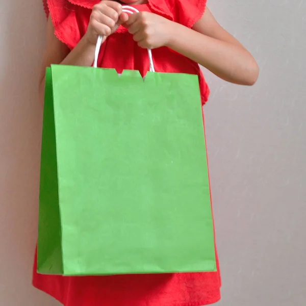 Una niña pequeña con un paquete en su hend disfruta de compras y venta sobre un fondo claro. Niño de buen humor —  Fotos de Stock