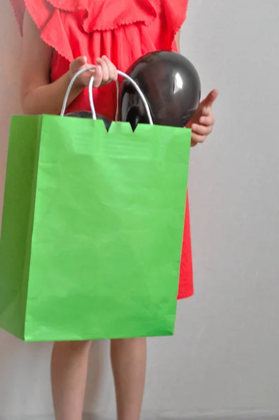 A little girl with a package in her hend enjoys shopping and sale on a light background. Child in good mood — Stock Photo, Image