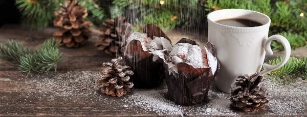 Christmas Breakfast of two cupcakes and a Cup of hot coffee sprinkled with powdered sugar, on the background of fir branches with lights. — Stock Photo, Image
