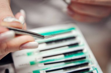 Kirpik uzatma yordamı. Kadın elle Closeup kirpik uzatma için aracı. Cımbız üstadı çalışıyor.