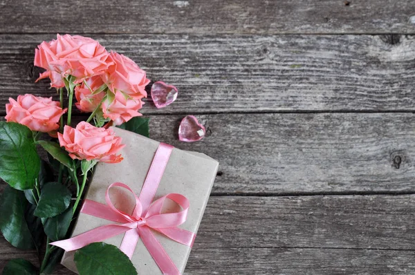 Zarter Korallenschatten rosa Rosen und Geschenk mit Herz und Briefkopf auf rustikalem Holzgrund. Valentin-Hintergrund. Urlaubskarte für Frauen — Stockfoto