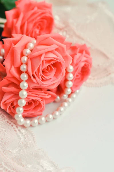 Délicat thème féminin. Rosiers rose corail tendance couleur sur un soutien-gorge rose pâle et collier de perles sur un fond blanc. vue de dessus. de près. Élégant plat de lingerie laïc. Concept de mode sous-vêtements — Photo