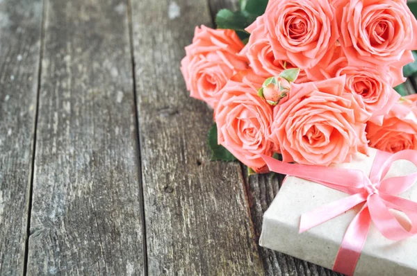 Zarte Korallen Schatten rosa Rosen und Geschenk auf rustikalem Holzhintergrund. Valentin-Hintergrund. Urlaubskarte für Frauen — Stockfoto