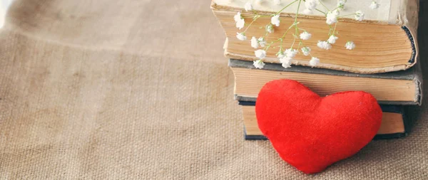 Vintage rustic love card for Valentines day-white flowers, yellowed old books and red plush heart on burlap. closeup. tinted. Shabby chic