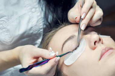 Kirpik uzatma yordamı. Kadın elle Closeup kirpik uzatma için aracı. Cımbız üstadı çalışıyor.