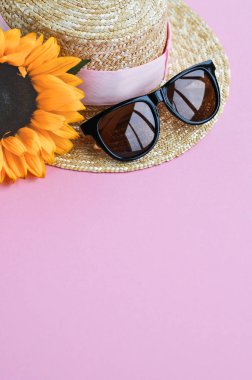 Pembe arka planda yaz hasır şapka, güneş gözlüğü ve ayçiçeği. yakın çekim.