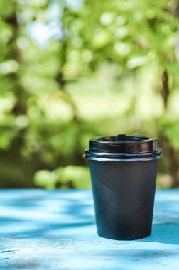 Yeşil çim ve güneş ışığına karşı mavi ahşap bir bankta Siyah karton kahve Fincan. Mockup.