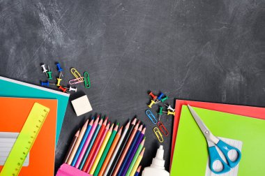 Siyah bir Tahta arka plan defterleri, kalemler, makas ve diğerleri parlak kırtasiye. Kavram okula geri