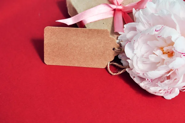 Rosa Pfingstrose Blume neben Geschenkbox auf rotem Hintergrund. — Stockfoto