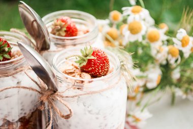 Rustik bir tarzda piknikte çilek, Chia ve granola ile yoğurt tatlısı ile cam bir kavanoz.