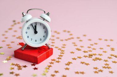 Tatil zamanı için pembe narin arka plan üzerinde kırmızı hediye ve yıldız konfeti ile beyaz çalar saat.