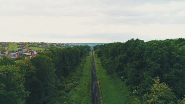 Vista aérea, movendo-se para baixo, mantém em foco a ferrovia e mostra área rural maravilhosa, no fundo da floresta verde . — Vídeo de Stock