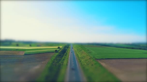 Vista aérea borrosa de diferentes tipos de coches que conducen a lo largo de la carretera de grava vacía a través de prados verdes y campos agrícolas paisaje. 4K . — Vídeos de Stock