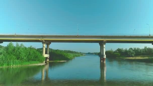 静かな川に架かる橋道に沿って速く移動する車の航空写真。4k. — ストック動画