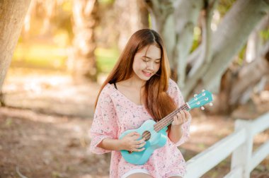 Yaz aylarında şapka oyun ukulele Bossanova müzik ile Asya Bayan. Genç Sevimli kadın açık havada müzik oynuyor. Mutlu bir genç kız bir ağacın altında ukulele oynarken hoşlanır. 