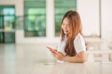 Kadın yazarak yazma iletide modern bir kafede akıllı telefon. Kahve ya da cep telefonuyla cappuccino bir masada oturan genç güzel kız Resim kırpılmış.