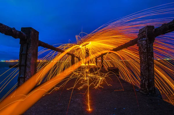 Showers of hot glowing sparks from spinning steel wool.Fire dancing show at twilight.Burning Steel Wool spinning. Hot Golden Sparks Flying from Man Spinning Burning Steel Wool on Wooden Bridge Extend