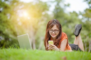 Açık hava parkında çalışan genç ve güzel bir Asyalı kadın. İyi istirahatler. Sahibi iş kadını açık hava parkında çalışıyor. İnternet ve teknoloji konsepti..