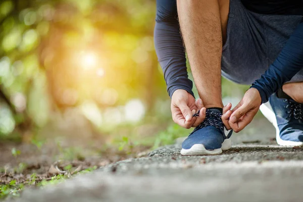 Man tying jogging shoes.A person running outdoors on a sunny day.Focus on a side view of two human hands reaching down to a athletic shoe.Young male jogger athlete training and doing workout outdoors