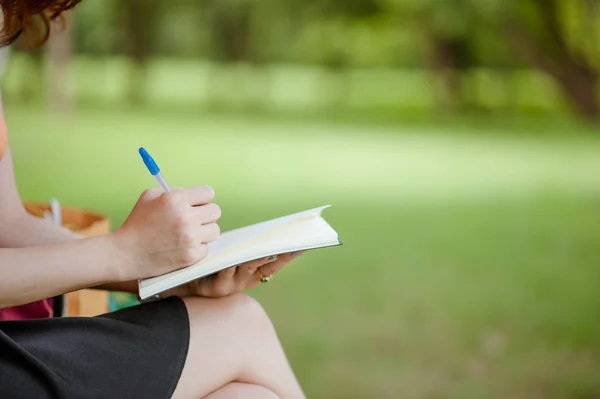 女の子は公園でノートにペンを書いて手を 夏の日にスイングとライティングに座っているアジアの女の子 教育の概念 — ストック写真
