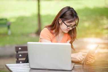 Açık hava parkında çalışan genç ve güzel bir Asyalı kadın. İyi istirahatler. Sahibi iş kadını açık hava parkında çalışıyor. İnternet ve teknoloji konsepti..