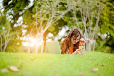 Açık hava parkında çalışan genç ve güzel bir Asyalı kadın. İyi istirahatler. Sahibi iş kadını açık hava parkında çalışıyor. İnternet ve teknoloji konsepti..