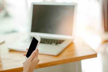 El ele tutuşan akıllı telefon siyah ekran Ve arkasında bir laptop.