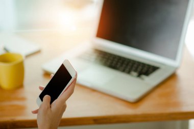 El ele tutuşan akıllı telefon siyah ekran Ve arkasında bir laptop.