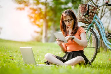 Genç ve güzel Asyalı bir kadın internette / laptopta çalışıyor açık hava parkında alışveriş yapıyor..
