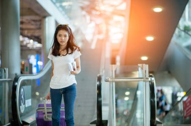 Modern havaalanı terminalinde bavulu çeken genç bir kadın. Taşıyıcıyı beklerken bavuluyla gezen adam. Dikiz aynası. Boşluğu kopyala