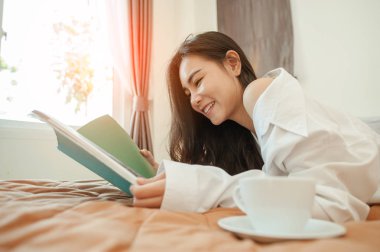  Kadın kitap okuyor ve yatakta kahve içiyor..