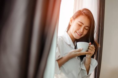 Elinde bir fincan kahve tutan bir kadın. Penceresinde güneş doğarken evde kahve içen bir kadın. .