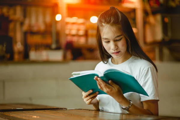 Young woman in a restaurant reading a book.girl sitting by wooden table and reading book