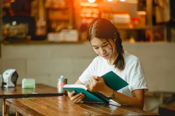 餐馆里的年轻女人在看书 女孩坐在木桌边看书 — 图库照片