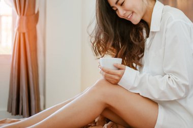 Elinde bir fincan kahve tutan bir kadın. Pencerede gün doğumuyla evde kahve içen bir kadın..