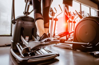 Bir eliptik üzerinde kardiyo çalışmasının yakın bacağı. İnsanlar spor salonunda eliptik bir antrenörle çalışıyor. 