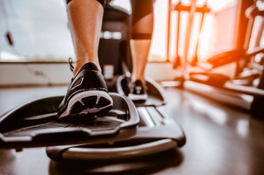 Bir eliptik üzerinde kardiyo çalışmasının yakın bacağı. İnsanlar spor salonunda eliptik bir antrenörle çalışıyor. 