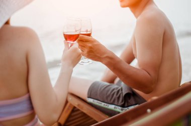 Aşıklar kumsalda geniş bardakları tokuşturuyor. Tropikal sahilde güneşli günün tadını çıkarıyorlar..