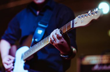 Sahne müzikal konserinde gitar çalan bir adam yakın çekim görüntüsü alıyor. Gitarist gitar çalıyor..