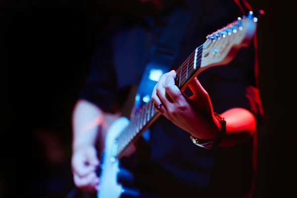 Sahne müzikal konserinde gitar çalan bir adam yakın çekim görüntüsü alıyor. Gitarist gitar çalıyor..