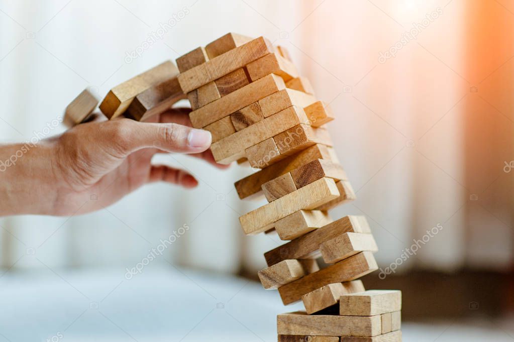 hand  pulling out or placing wood block on the tower in modern office. plan and strategy in business. blur for background.