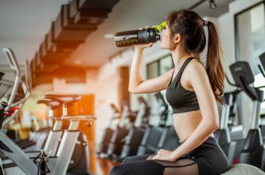 Spor salonunda yorgun olan genç fitness kadını protein içeceği. Egzersiz konsepti. Fitness ve sağlıklı yaşam tarzı. 