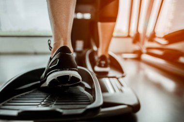 Bir eliptik üzerinde kardiyo çalışmasının yakın bacağı. İnsanlar spor salonunda eliptik bir antrenörle çalışıyor. 