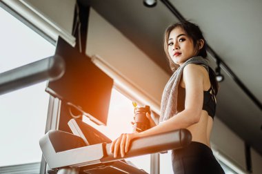 Koşu bandında su içen genç bir kadın. Koşu bandında protein içen genç bir kadın..