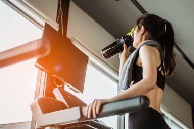 Koşu bandında su içen genç bir kadın. Koşu bandında protein içen genç bir kadın..